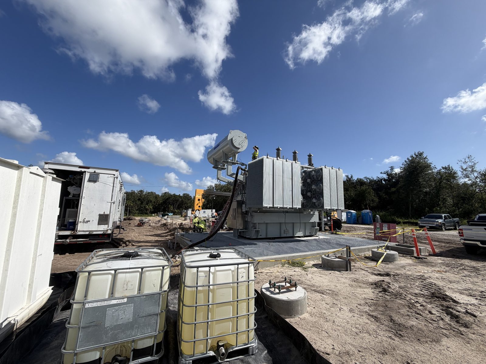 An 85 MVA Prolec generator step-up transformer on its pad at a new Florida solar site, with conservator, radiators, and bushings installed, the vacuum and oil processing trailer at left, and the crew on top of the tank.