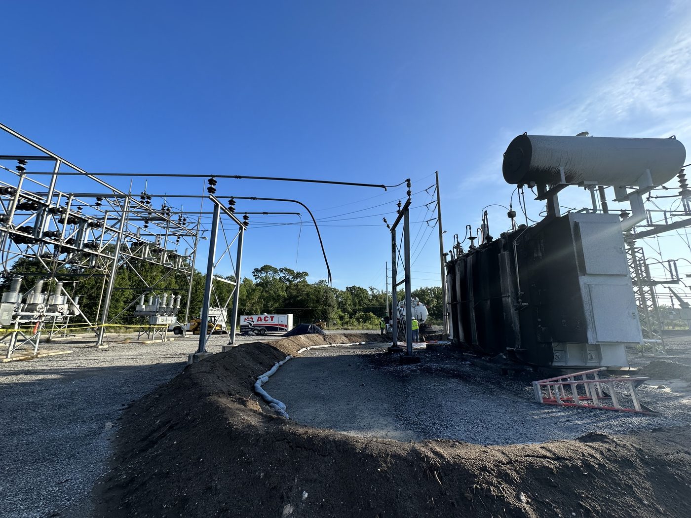 A 230 kV autotransformer failure site showing the replacement unit installed on the pad, scorched ground from the transformer fire, containment berms, and the bus structure that also required replacement.