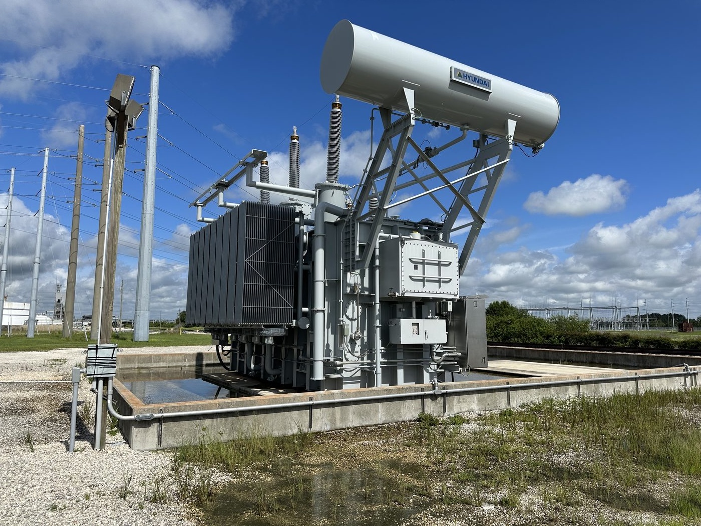A 230 kV Hyundai autotransformer in spare storage at a regional generating plant before disassembly. The conservator tank and support frame are visible, these had to be removed before transport.